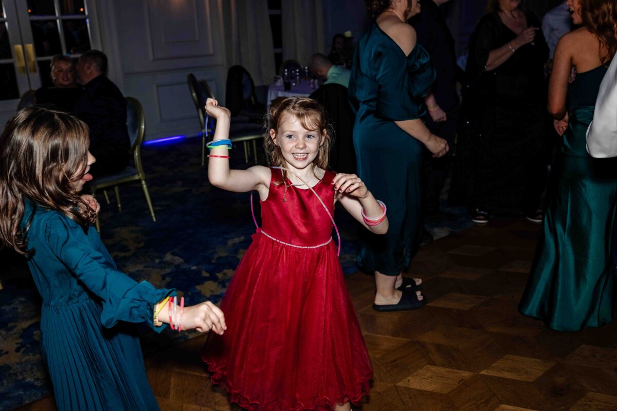 Little girl in a red dress laughing and dancing at the wedding reception on the dance floor