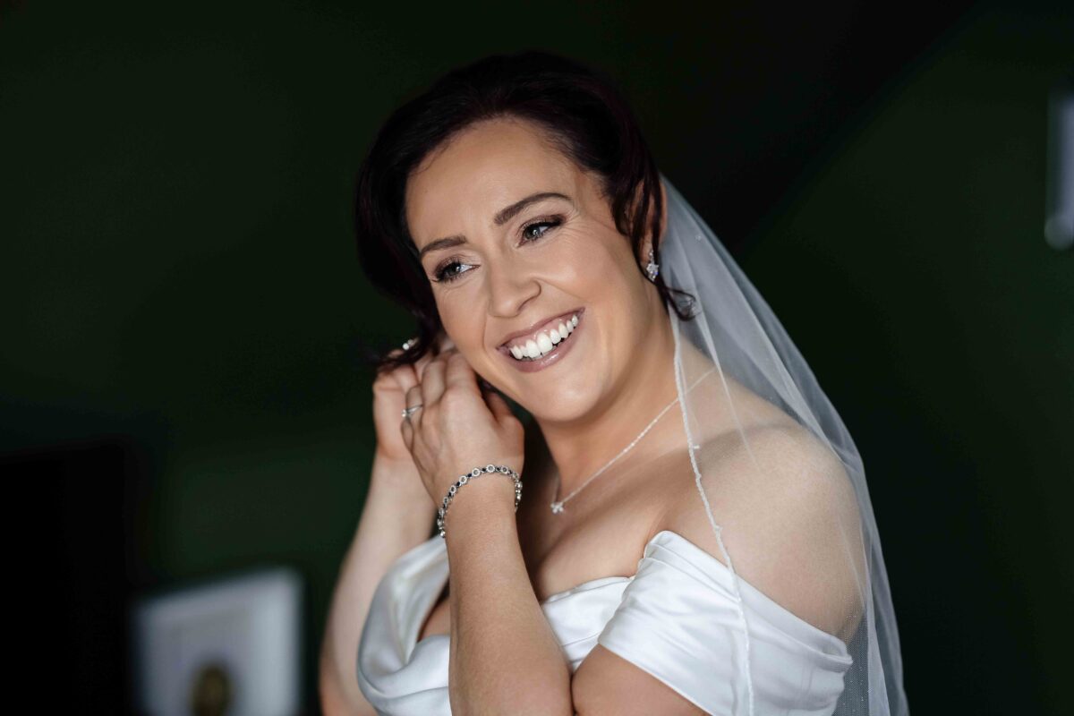 Smiling bride in a veil putting on an earring on the wedding morning