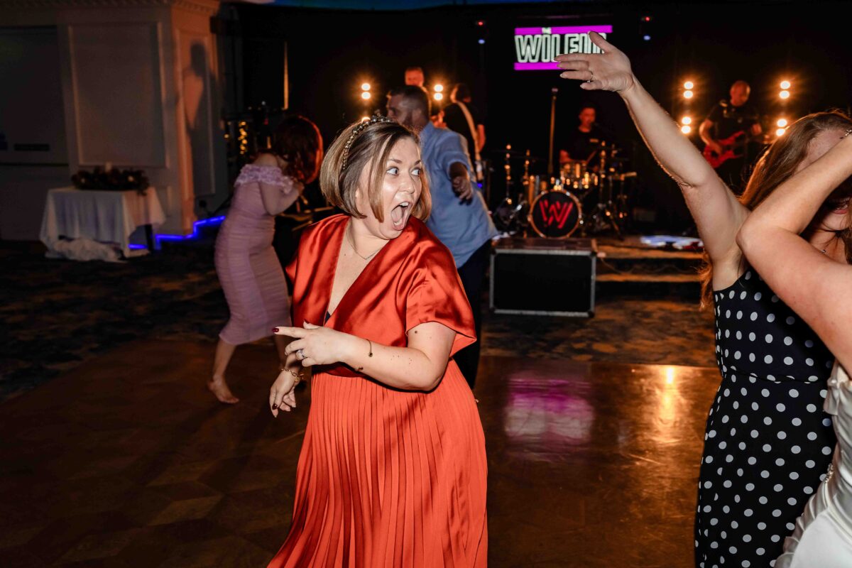 Wedding guest in an orange dress singing and dancing in front of the band The Wilful at Vienna Woods Hotel