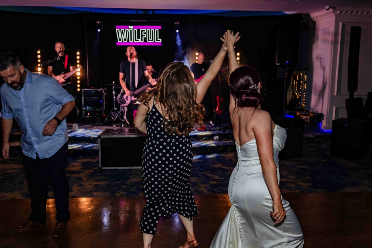 Bride in a fishtail wedding dress dancing with a guest in front of the live band at her Cork wedding reception