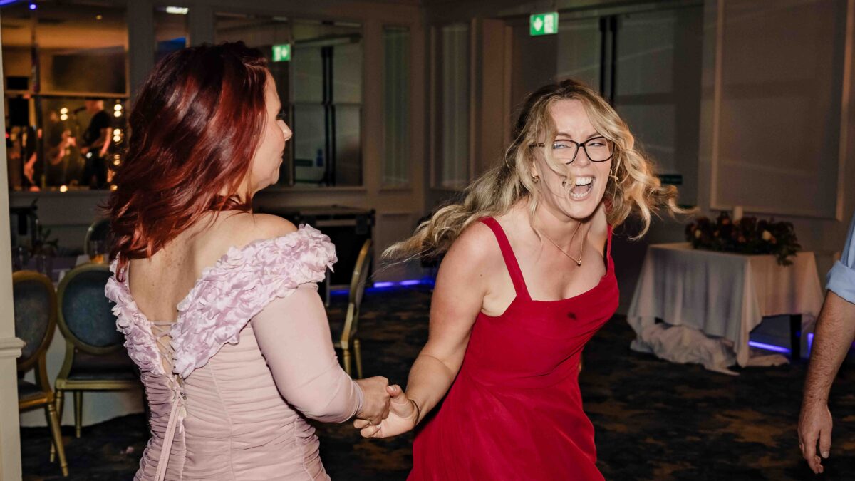 Two wedding guests holding hands and laughing as they spin on the dance floor at the evening reception