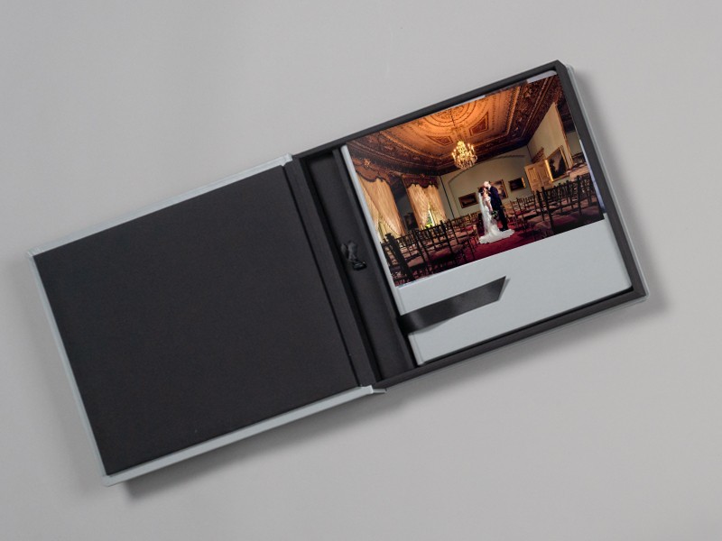 Open grey linen folio presentation box with a wedding photograph and black ribbon