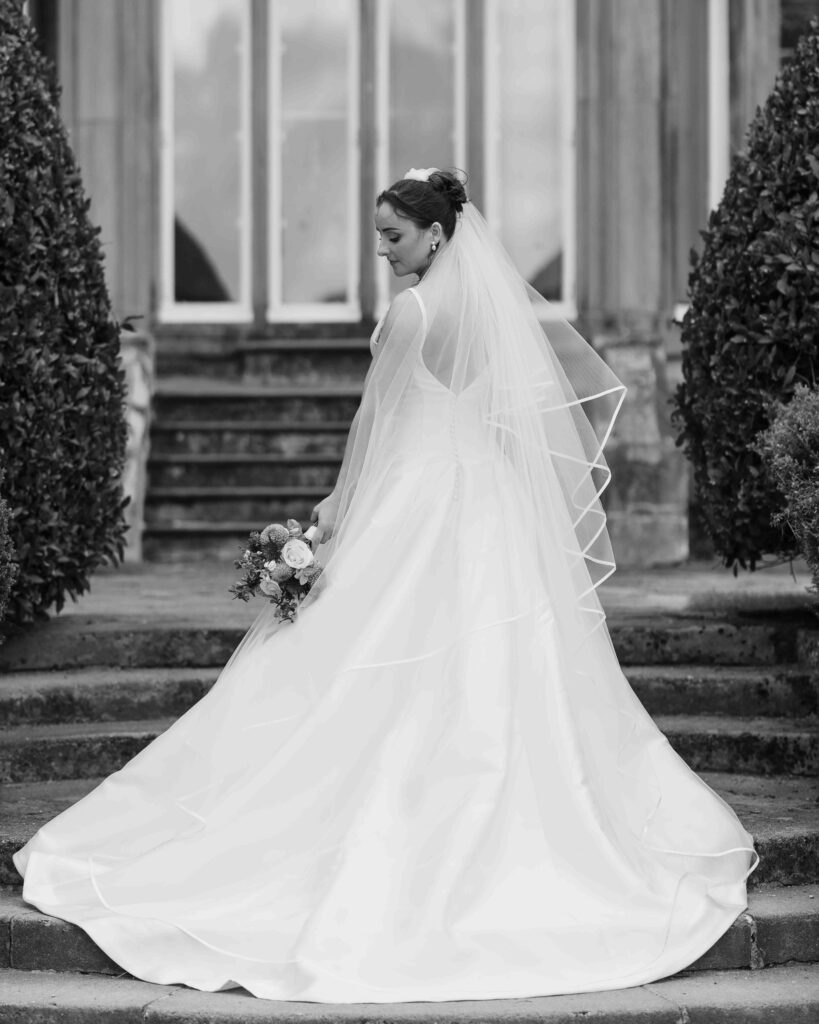 Black and white photo of the bride looking down at her long train and veil on stone steps in front of tall windows at Muckross House