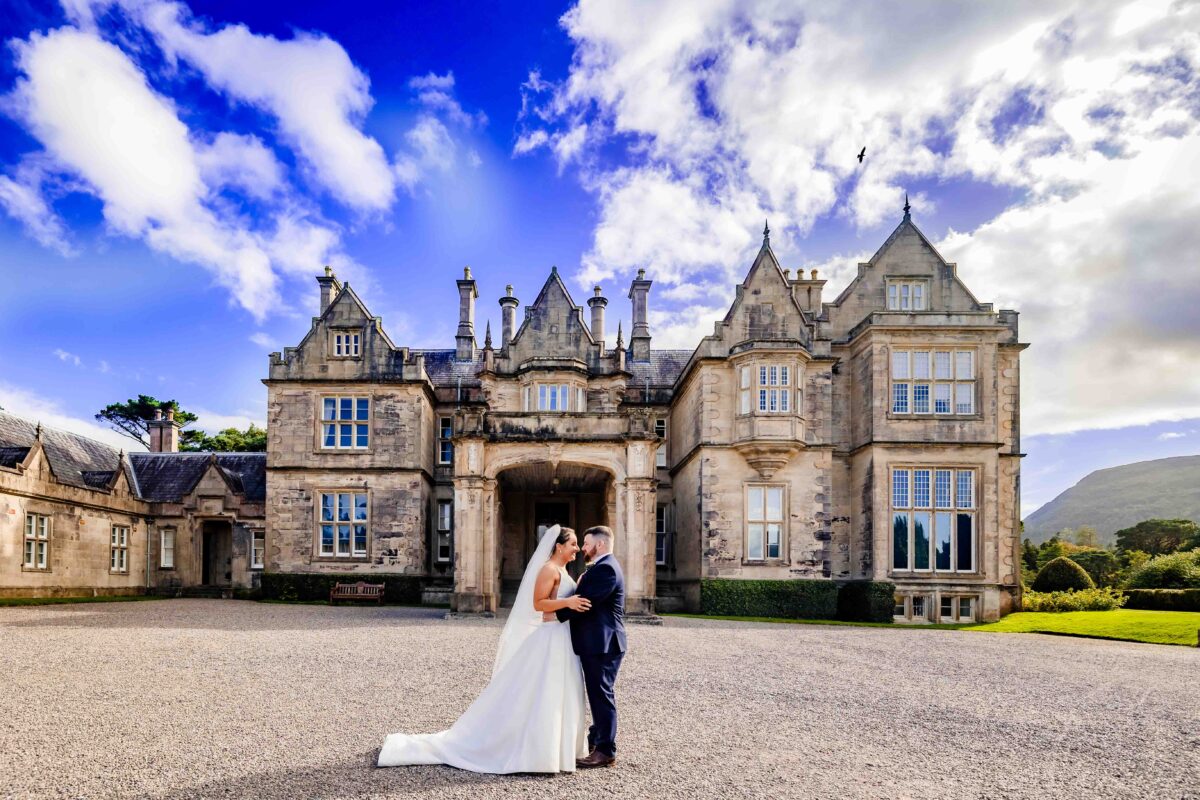 Wedding portrait in front of Muckross House, Killarney, Co. Kerry: bride and groom embracing with mountains and a blue sky behind