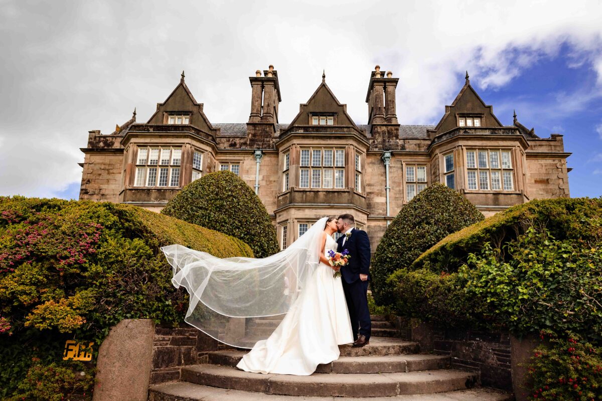 Bride and groom kissing on the stone steps at Muckross House in Killarney as the bride's long veil blows in the wind