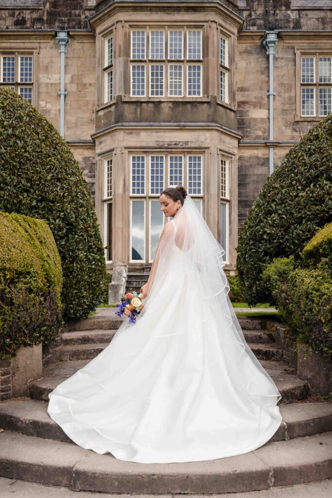 Bride in a long gown and veil on curved stone steps between clipped hedges at Muckross House, Killarney, Co. Kerry