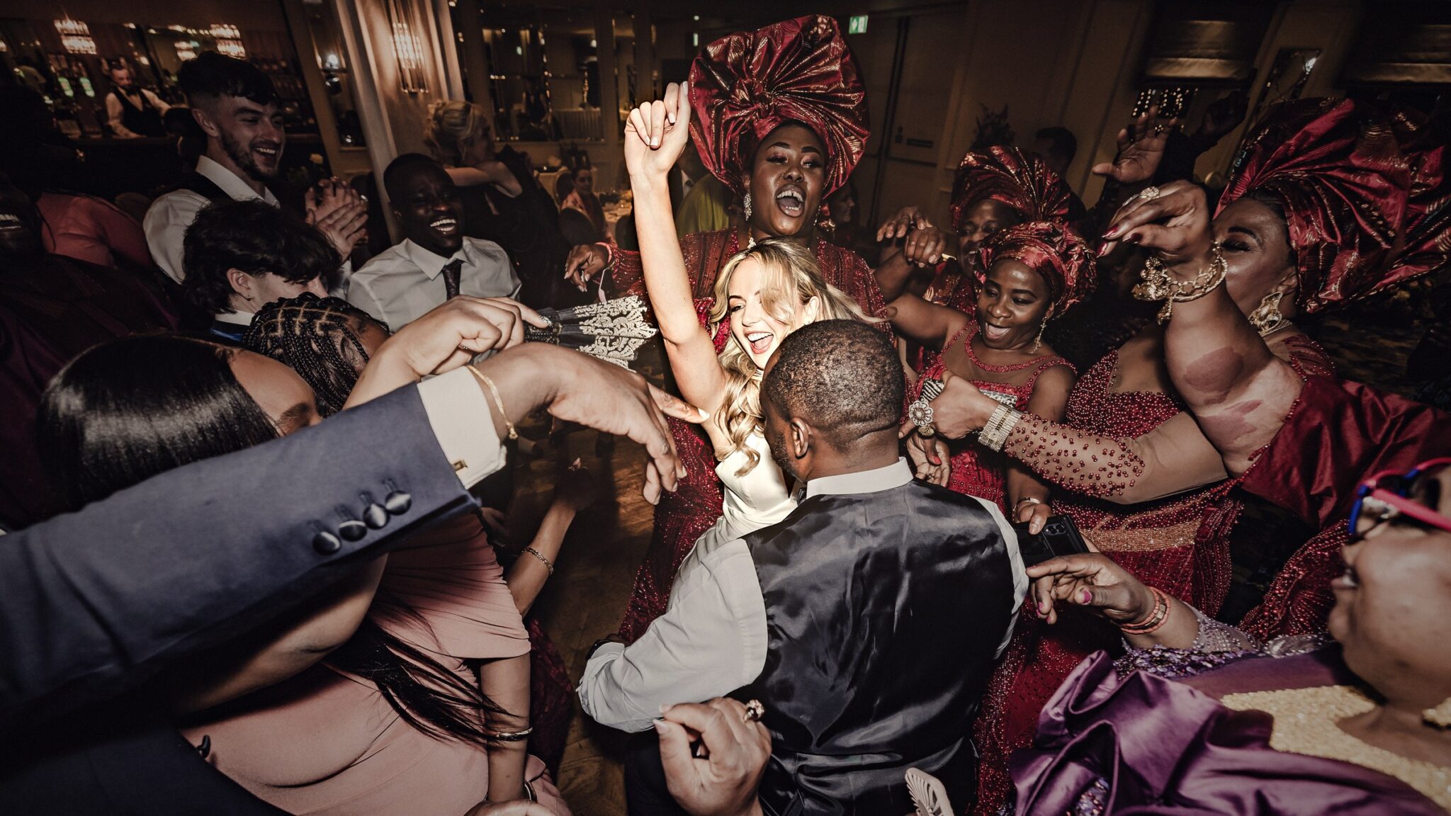 Stacey dancing in the middle of a circle of guests in red gele headwraps at an Irish and Nigerian wedding, Vienna Woods Hotel, Cork wedding photographer