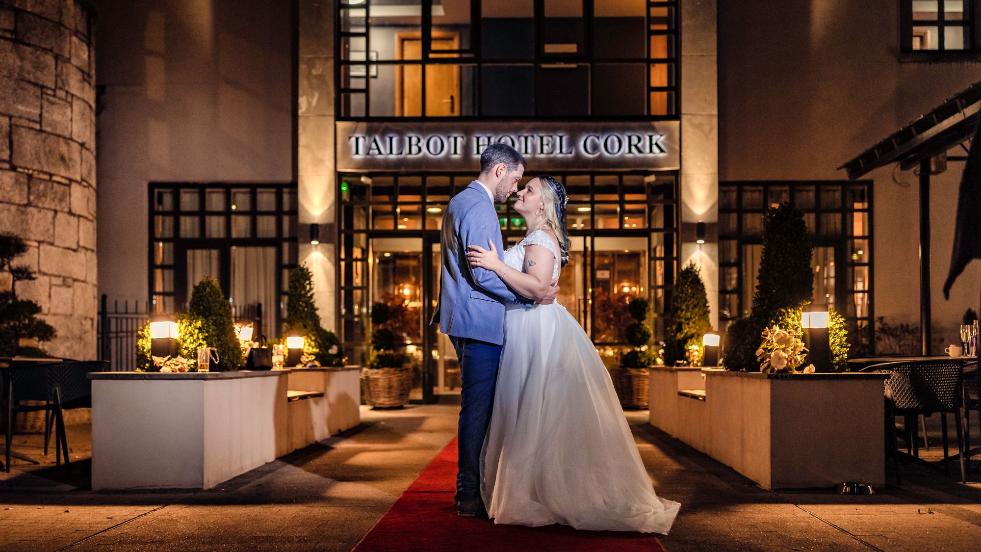 Shannon and Brandon embrace on the red carpet in front of the Talbot Hotel Cork at night, Talbot Hotel Cork wedding photographer