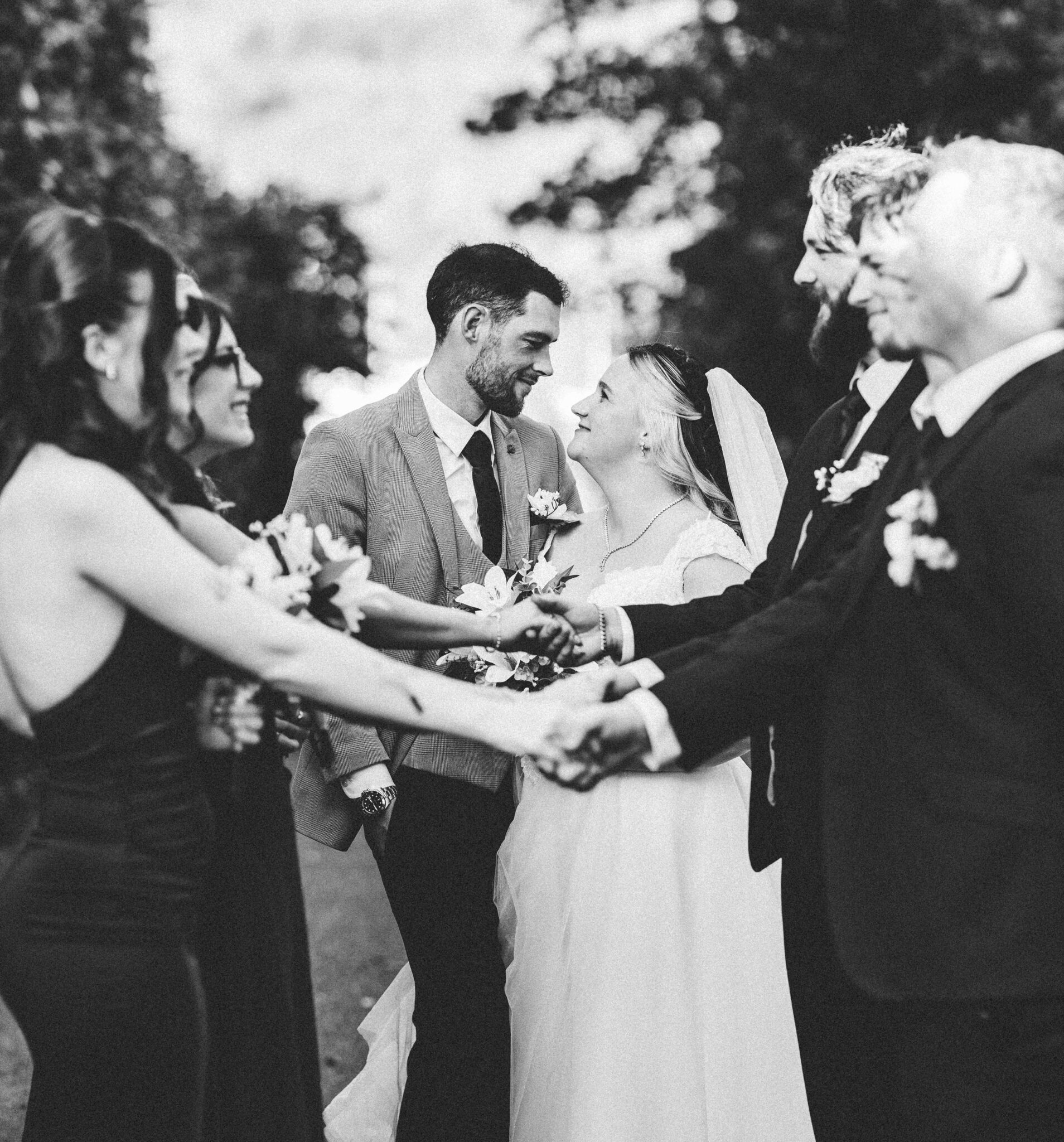 Black and white photo of friends and family joining hands around Shannon and Brandon at the Talbot Hotel Cork wedding