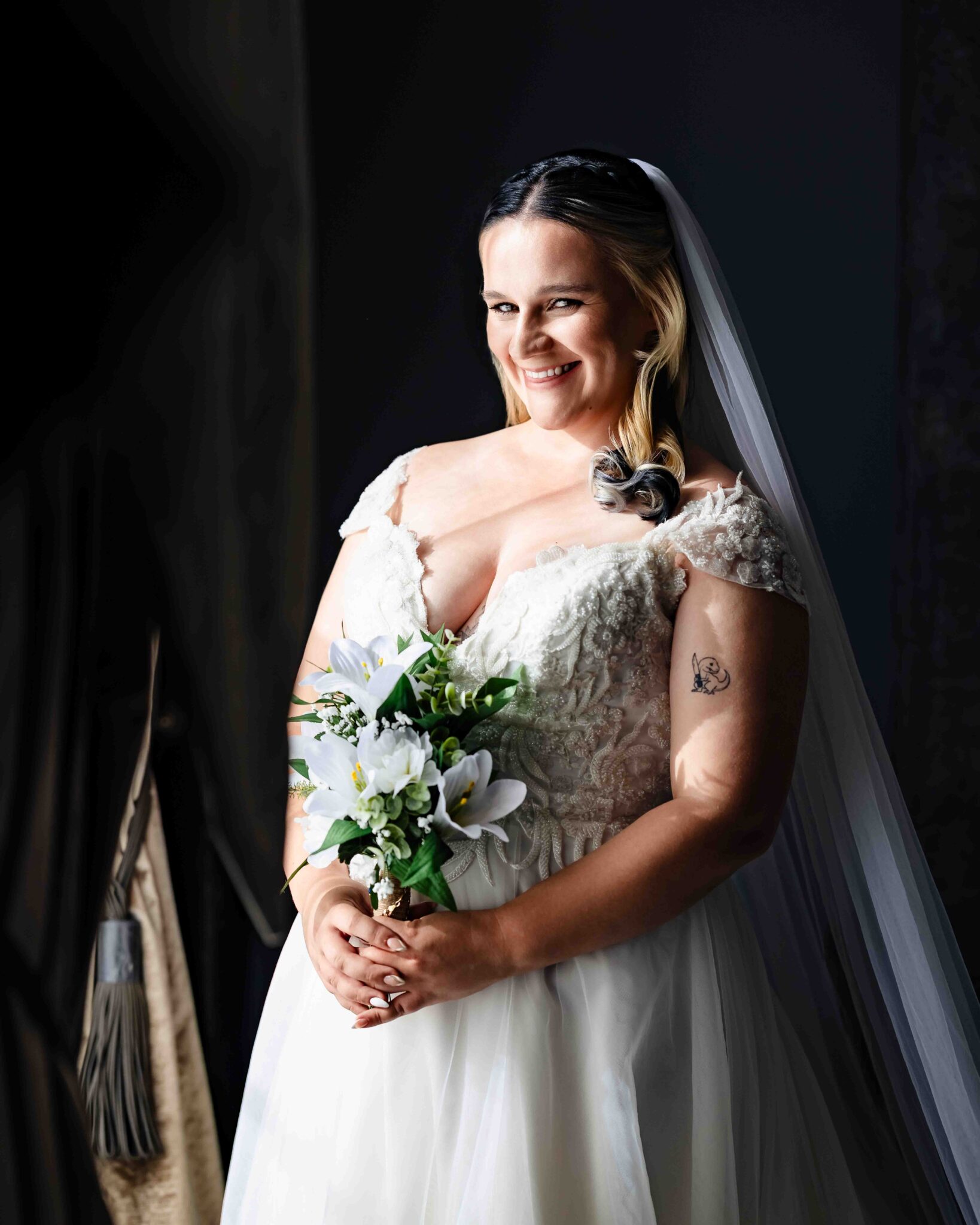 Shannon smiles in her wedding dress and long veil beside a dark window at the Talbot Hotel Cork, Cork wedding photography