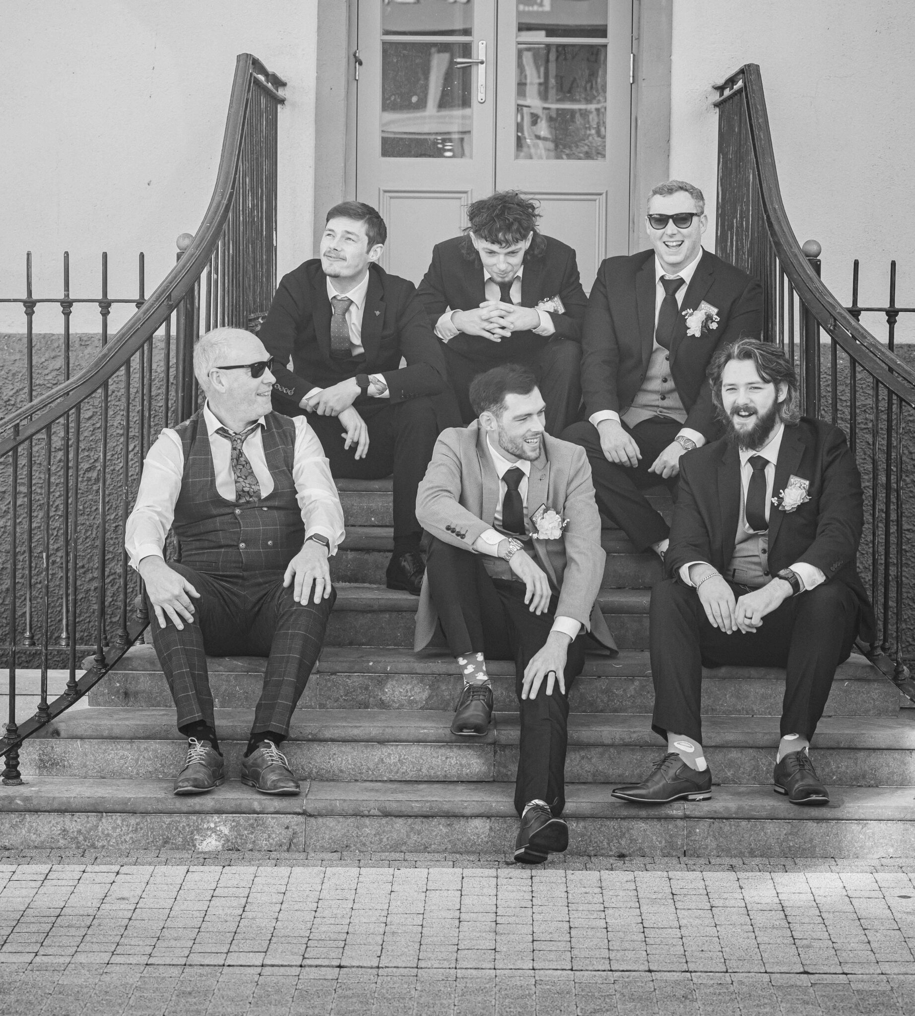 Black and white photo of Brandon and the groomsmen sitting on the steps outside the Talbot Hotel Cork