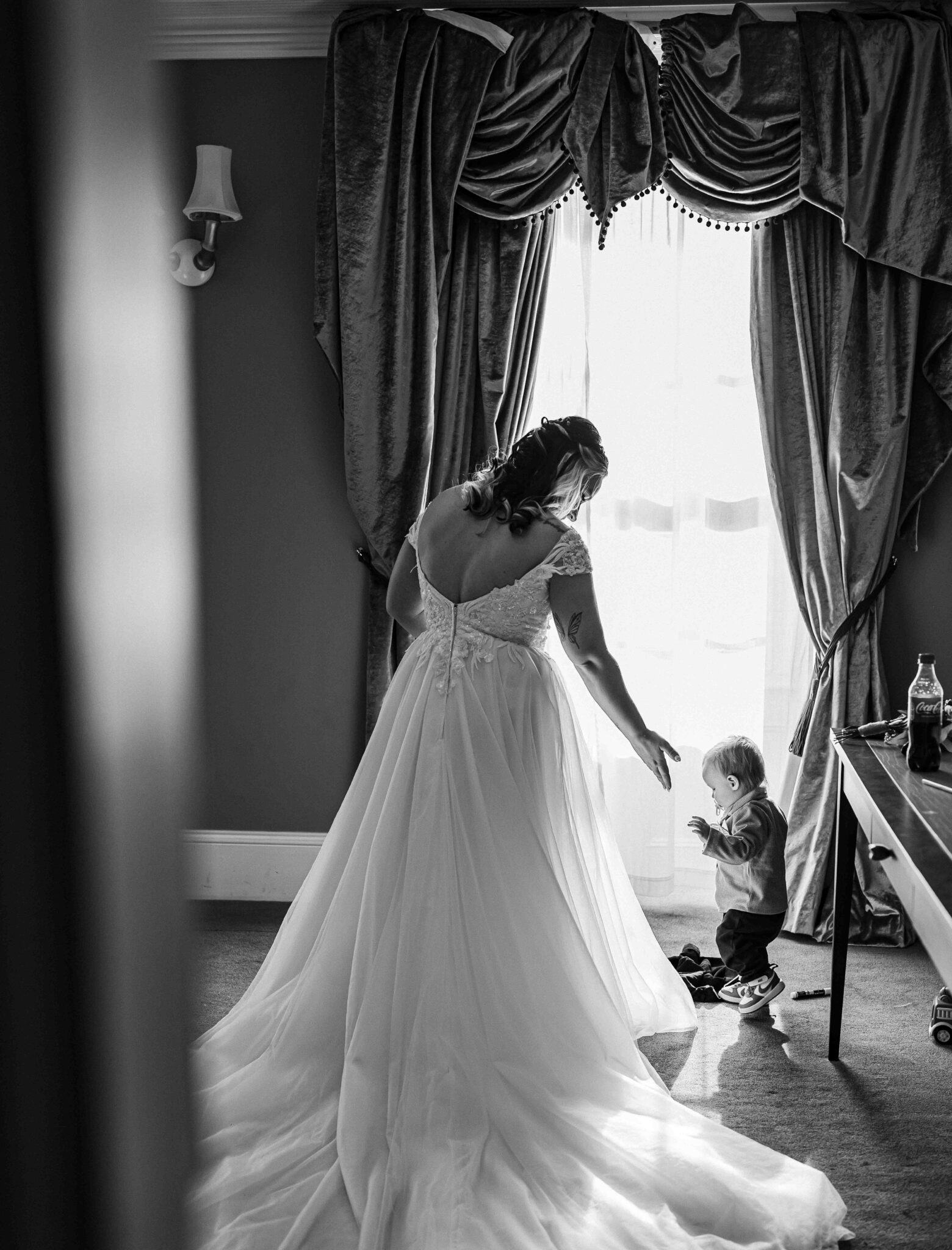 Black and white photo of Shannon in her wedding dress at the window while a toddler plays on the floor, Talbot Hotel Cork