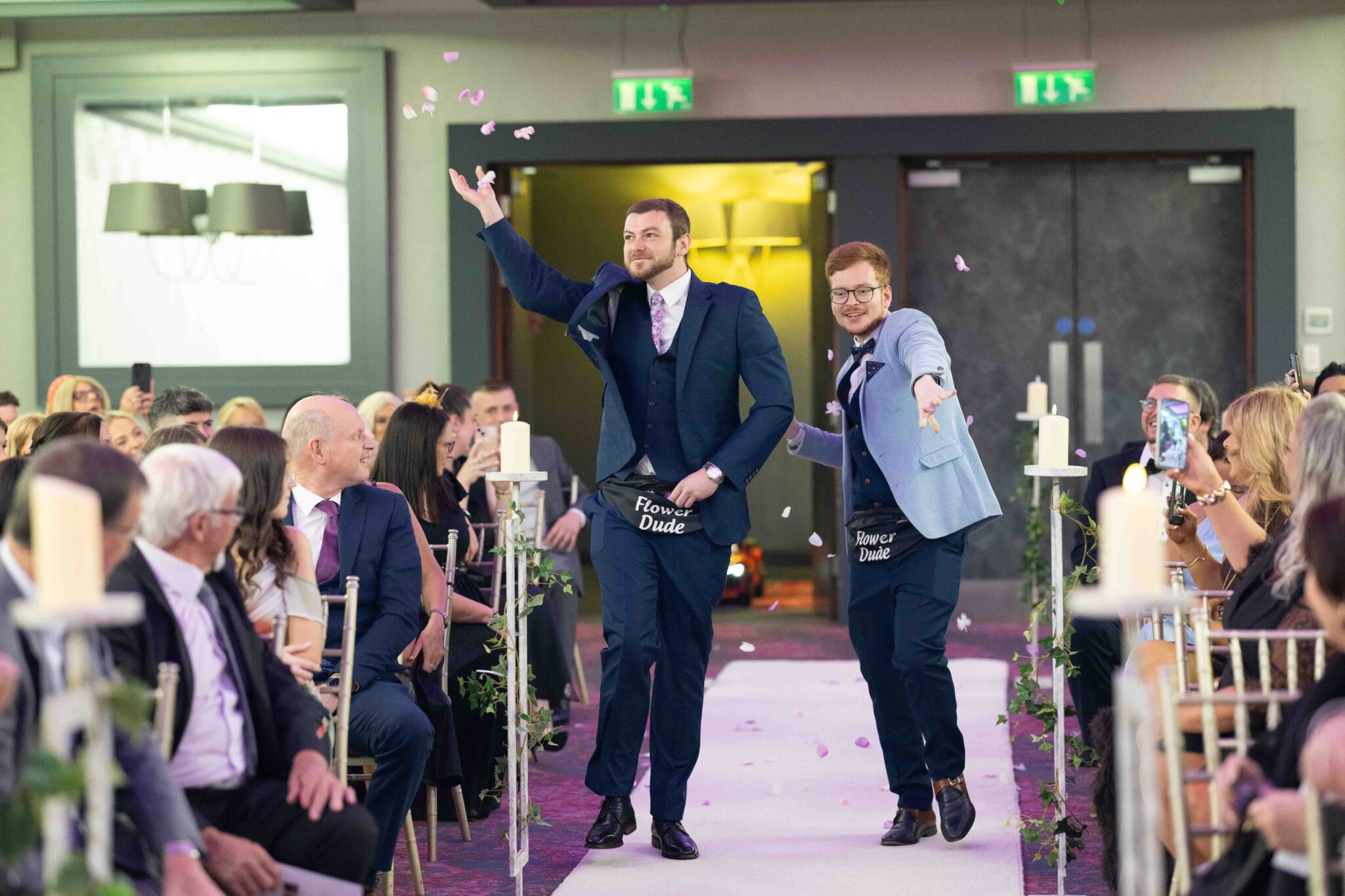 The Flower Dudes throw petals as they walk down the aisle at the Talbot Hotel Cork wedding, guests laughing