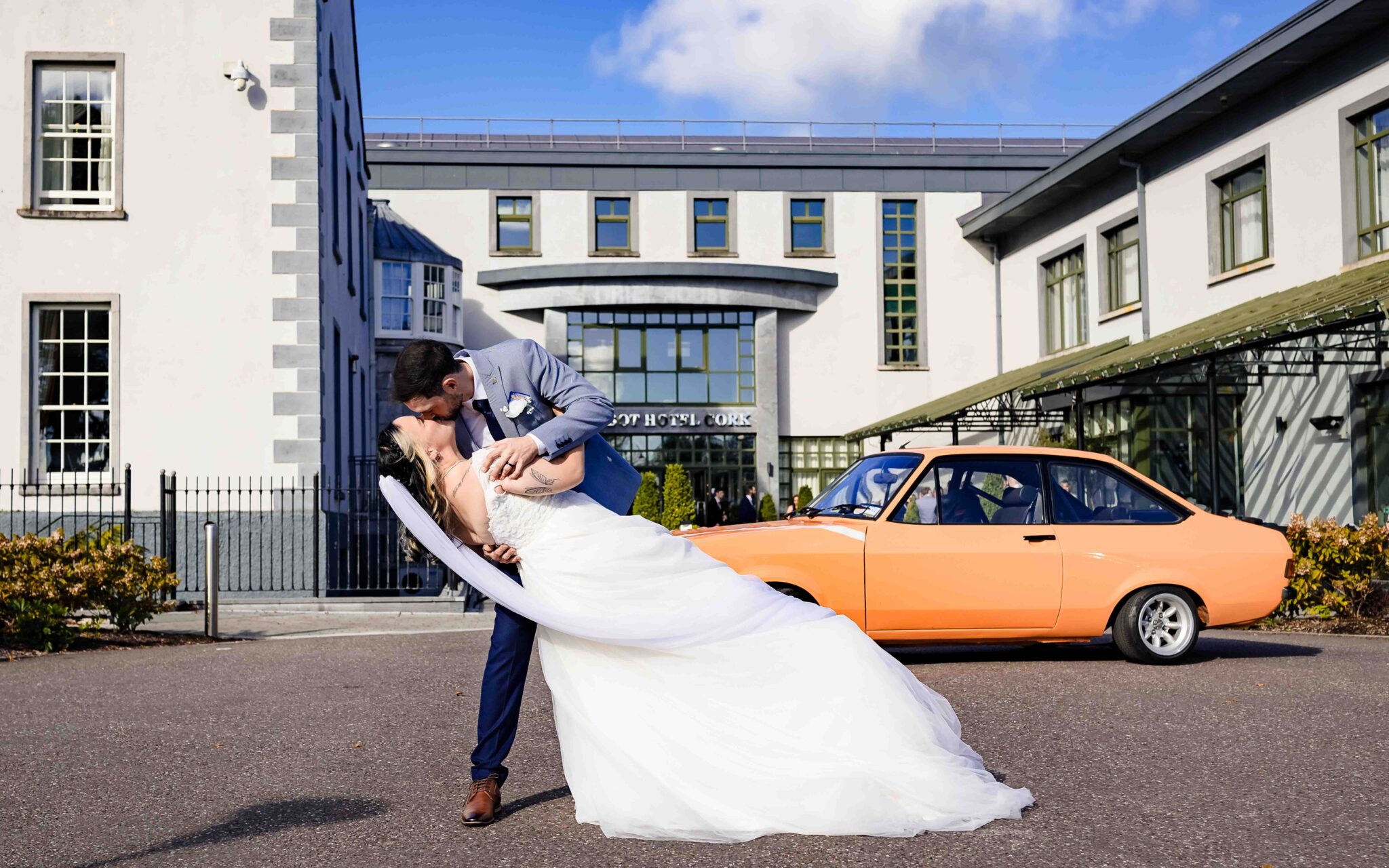 Brandon dips Shannon for a kiss in front of the Talbot Hotel Cork with a classic orange car, Talbot Hotel Cork wedding photographer