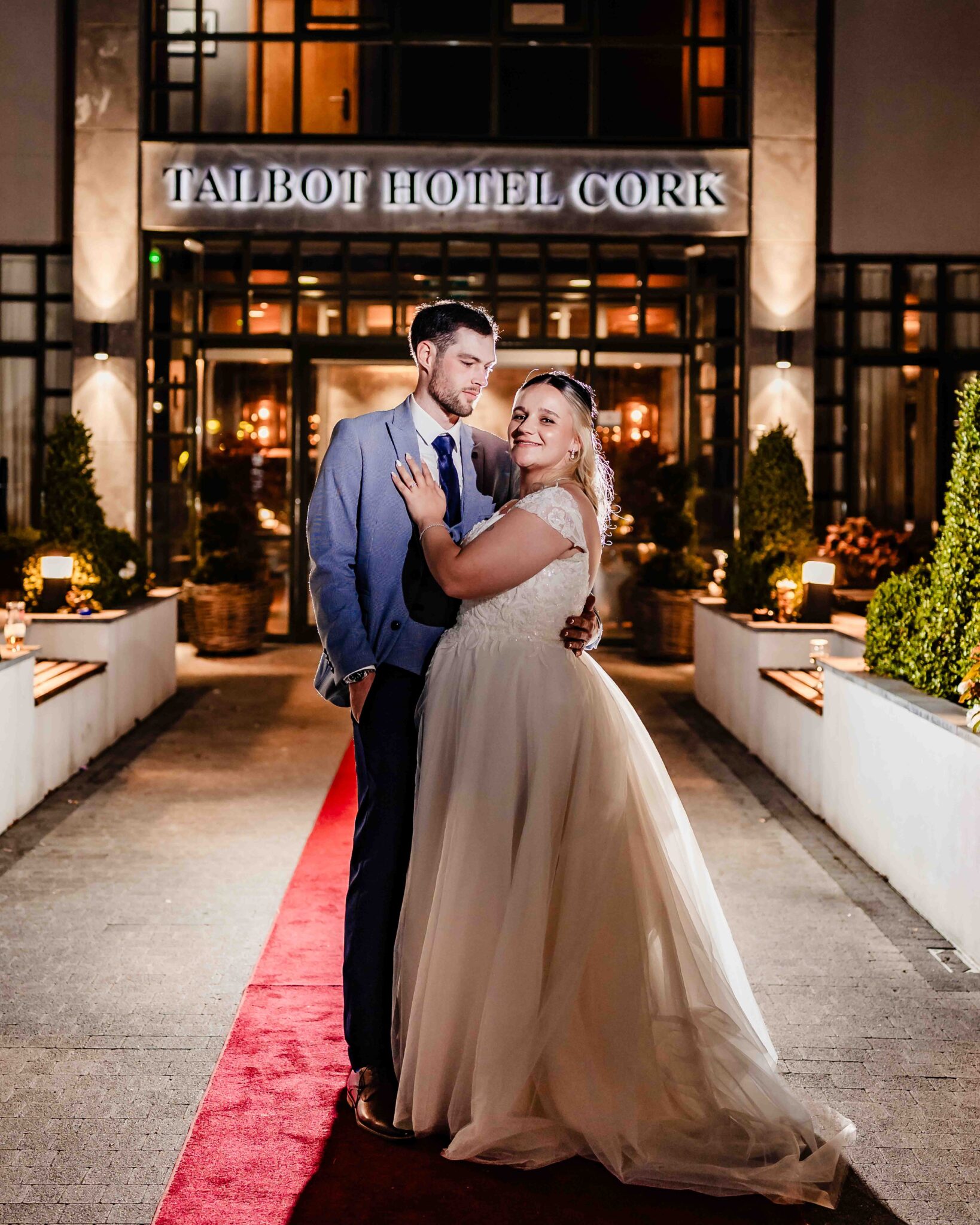 Shannon and Brandon embrace under the Talbot Hotel Cork sign on the red carpet at night, Talbot Hotel Cork wedding photographer