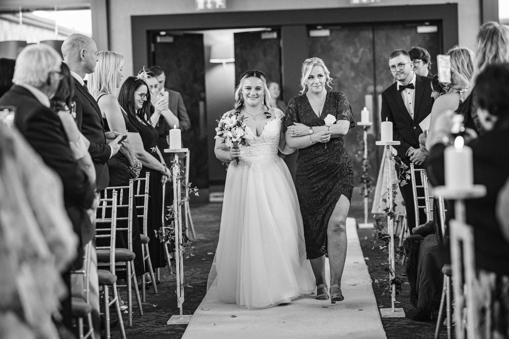 Black and white photo of Shannon walking up the aisle with a huge smile at the Talbot Hotel Cork wedding ceremony