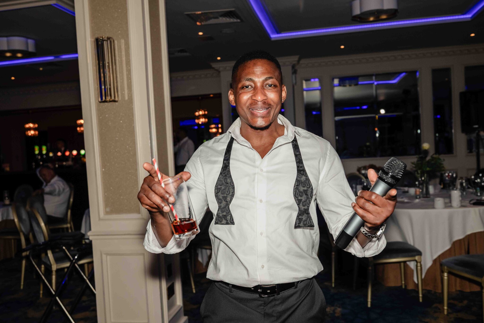 Wedding guest in an open bow tie raises a drink and dances at Vienna Woods Hotel, Cork wedding