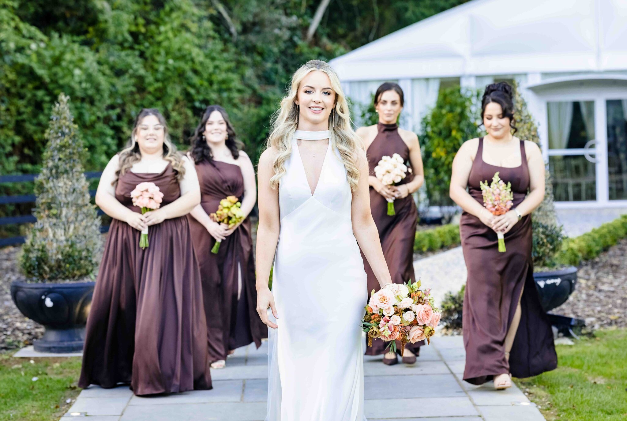 Bride walks with her bridesmaids carrying bouquets across the lawn at Vienna Woods Hotel, Cork wedding