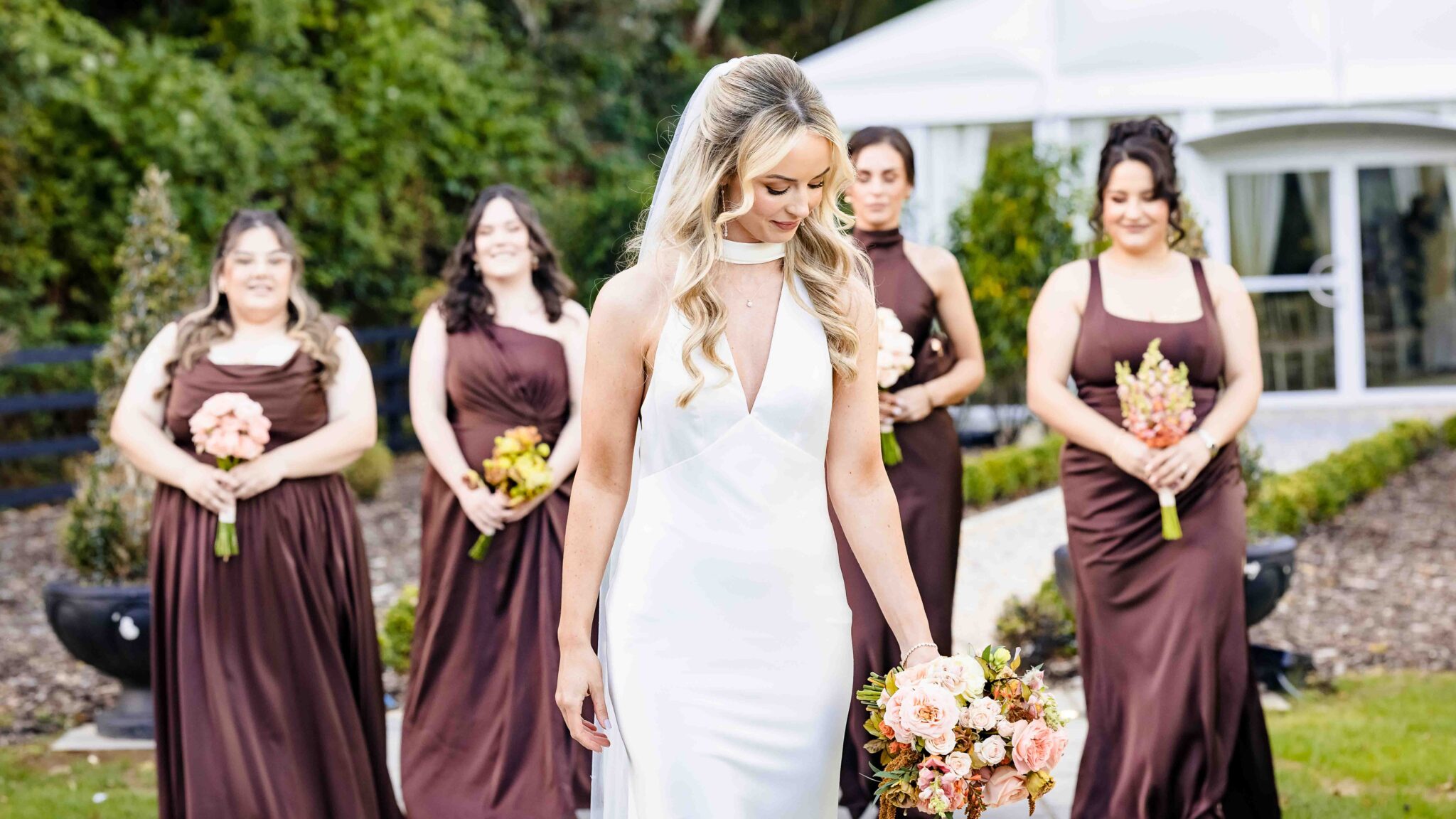 Bride looks down at her bouquet surrounded by bridesmaids in chocolate brown satin, Vienna Woods Hotel, Cork wedding photographer