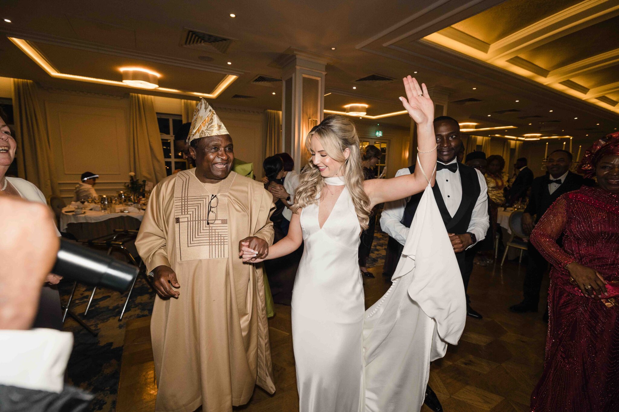 Bride dances with a guest in a gold Nigerian agbada at the Vienna Woods Hotel reception, Irish Nigerian wedding Cork