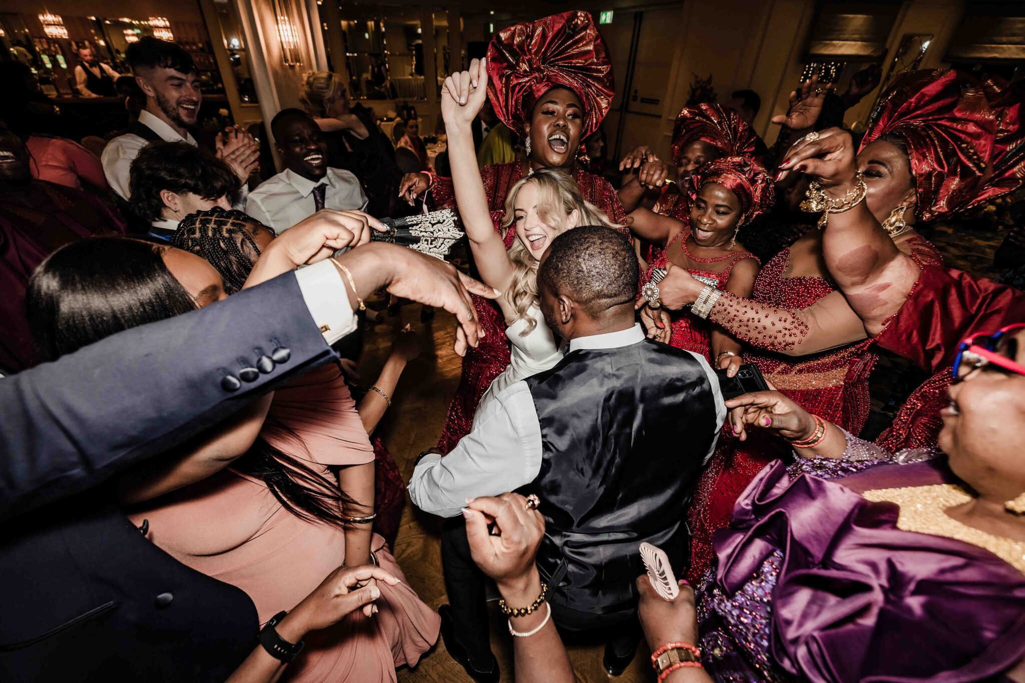 Stacey dances in a circle of guests in red gele headwraps at an Irish Nigerian wedding, Vienna Woods Hotel, Cork wedding photographer