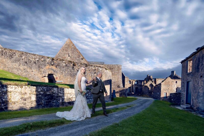 Bride and groom standing on rugged coastal cliffs at sunset – JOD Photography
