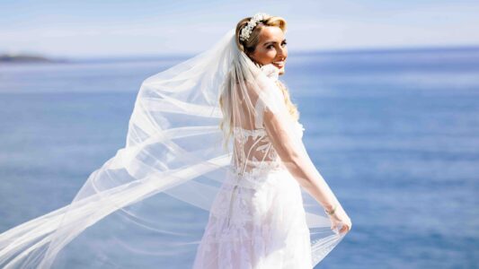 Dramatic wide-angle wedding portrait of a bride waving her long veil on the rocky shoreline of Long Strand beach near Clonakilty